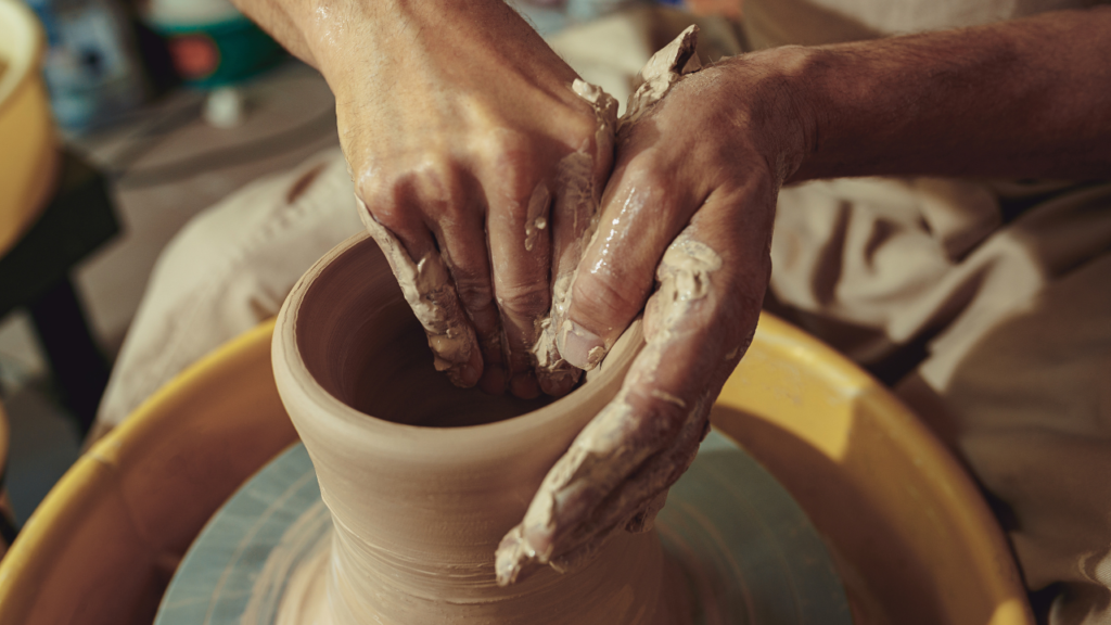 Close-up de mãos moldando argila em uma roda de oleiro.