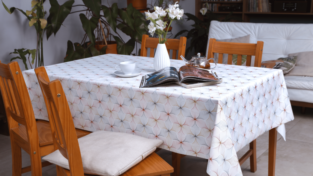 Uma mesa de jantar elegantemente decorada. A mesa é coberta por uma toalha de mesa de linho branca e adornada com um arranjo de flores. Um livro aberto completa a cena.