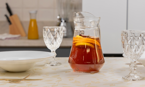 Foto de uma mesa pequena com uma jarra de vidro cheia de bebida e copos ao redor.